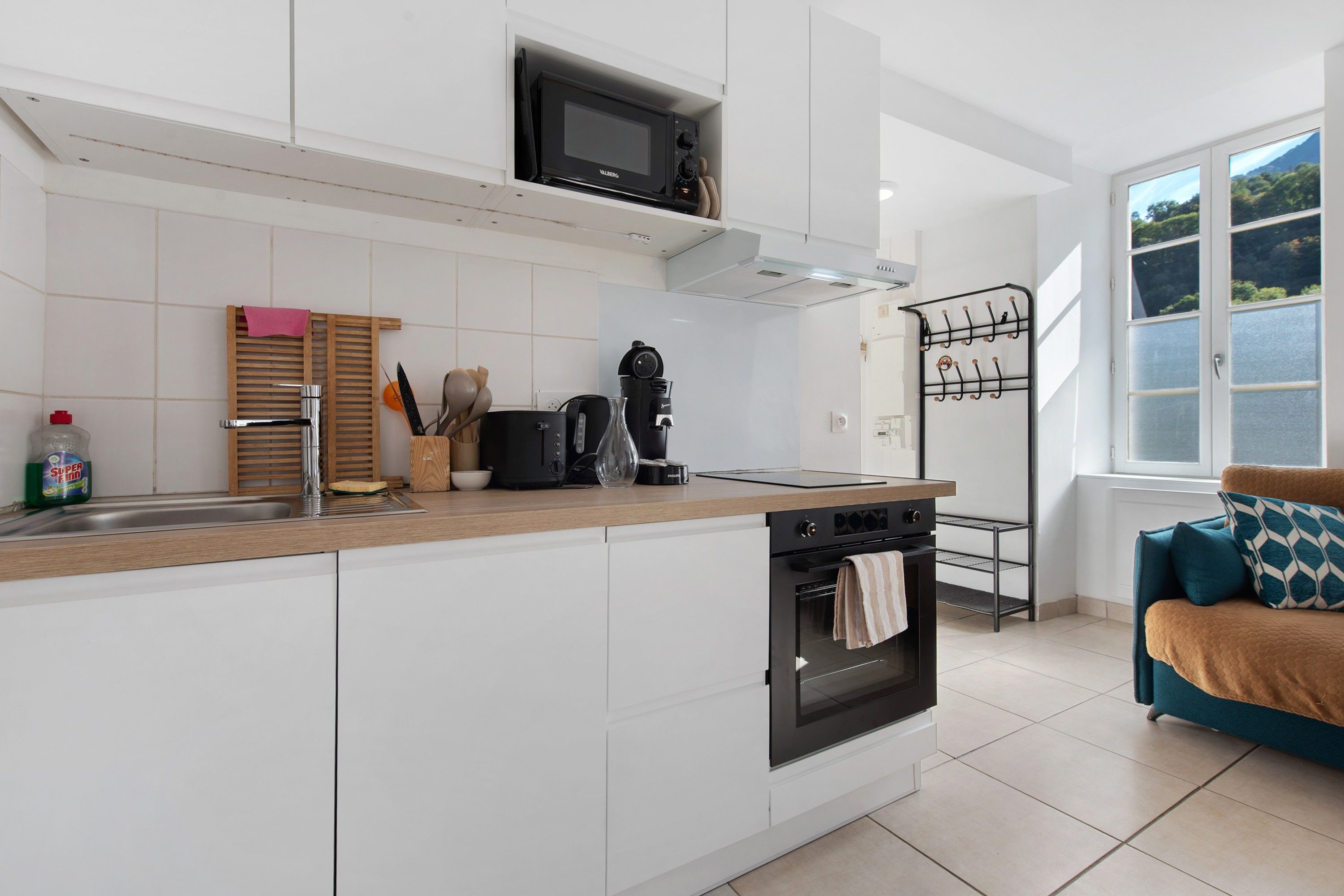 A modern kitchen with white cabinetry, a built-in microwave, and a stove. There is a window with a view of greenery outside.