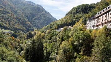 A mountainous landscape with dense forest and a row of buildings with multiple stories and balconies.