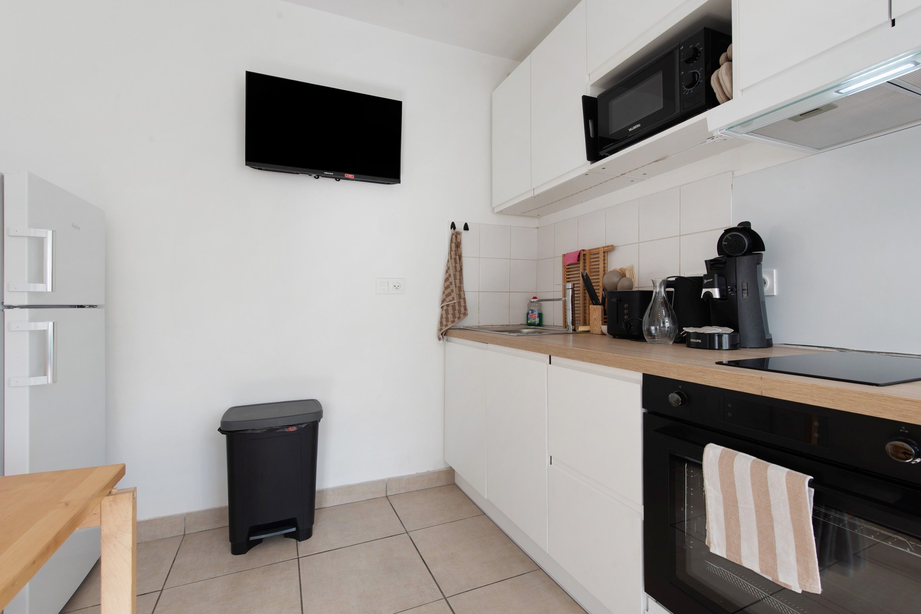 Een moderne keuken met witte kasten, een zwart aanrecht, een magnetron, een koffiezetapparaat en een prullenbak.