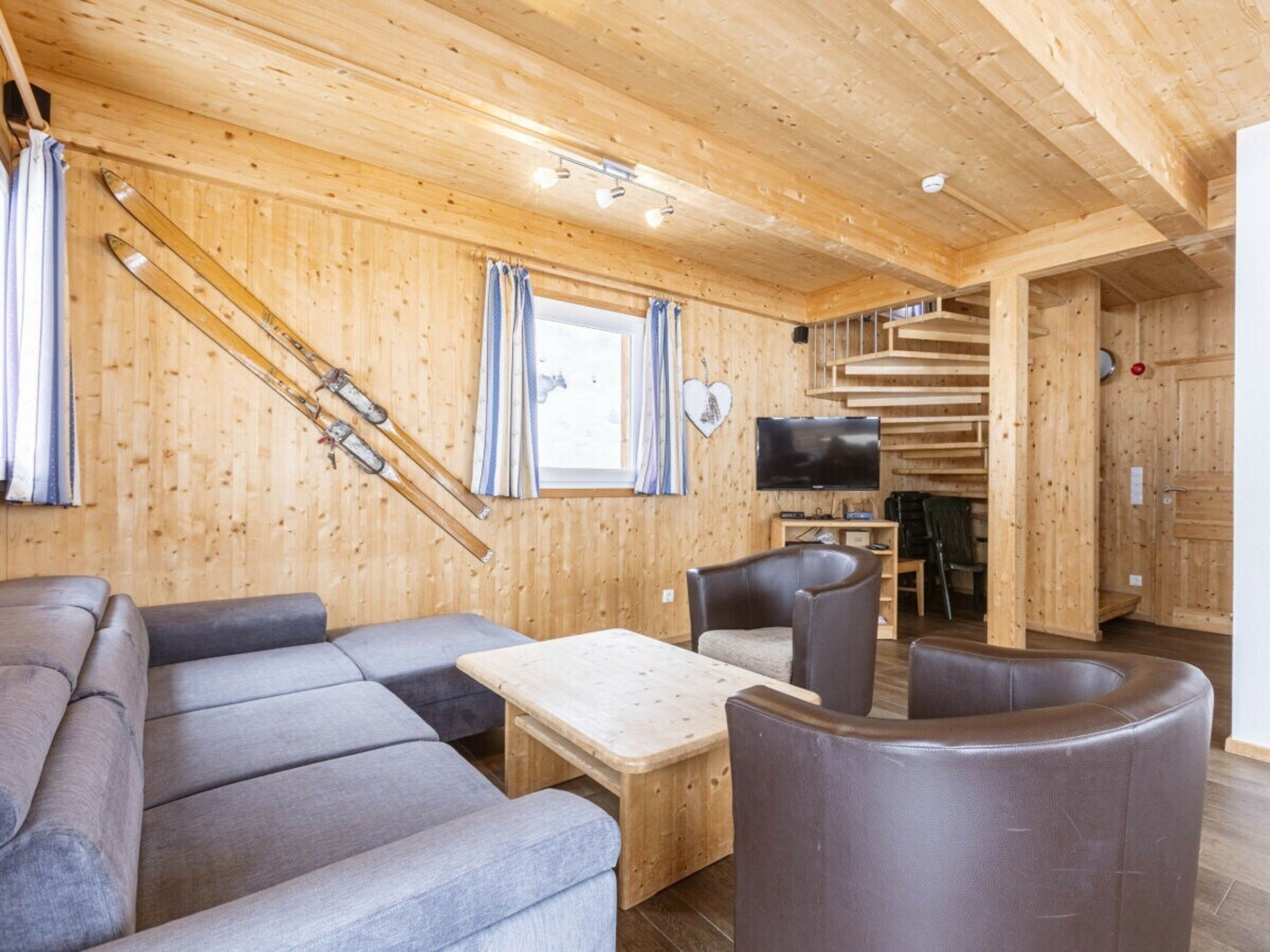 A wooden interior with a sofa, chairs, a table, a TV, and ski equipment.