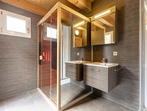 Een moderne badkamer met een douchecabine van glas, twee wastafels en een grote spiegel.
