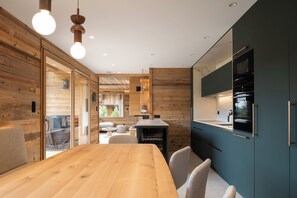 A modern kitchen with wooden cabinetry, a dining area with a wooden table, and a view into the living space. - ✨ Le Refuge de Lola – Family Chalet with Hot Tub, Games Room & Fireplace (Gérardmer)