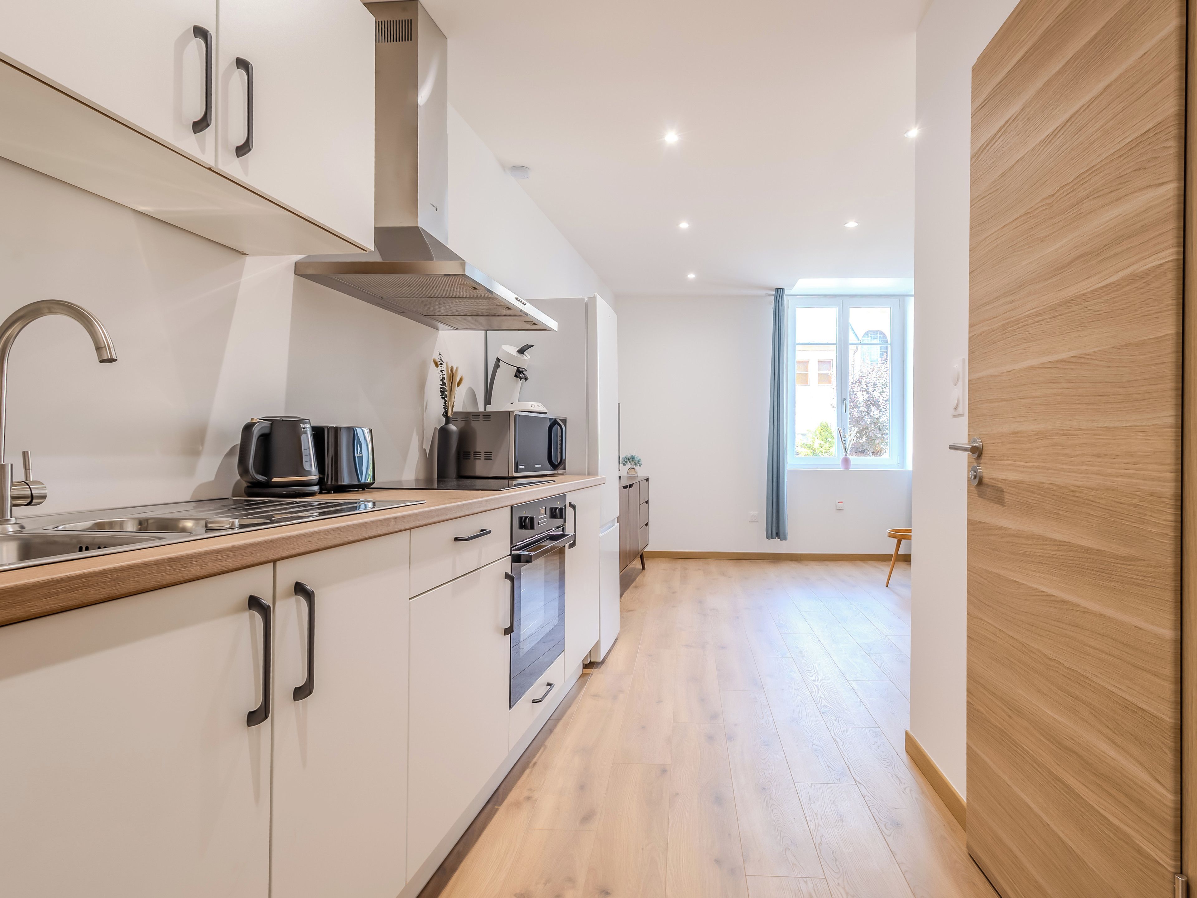 Una cocina moderna con extractor de acero inoxidable, horno empotrado y microondas.
