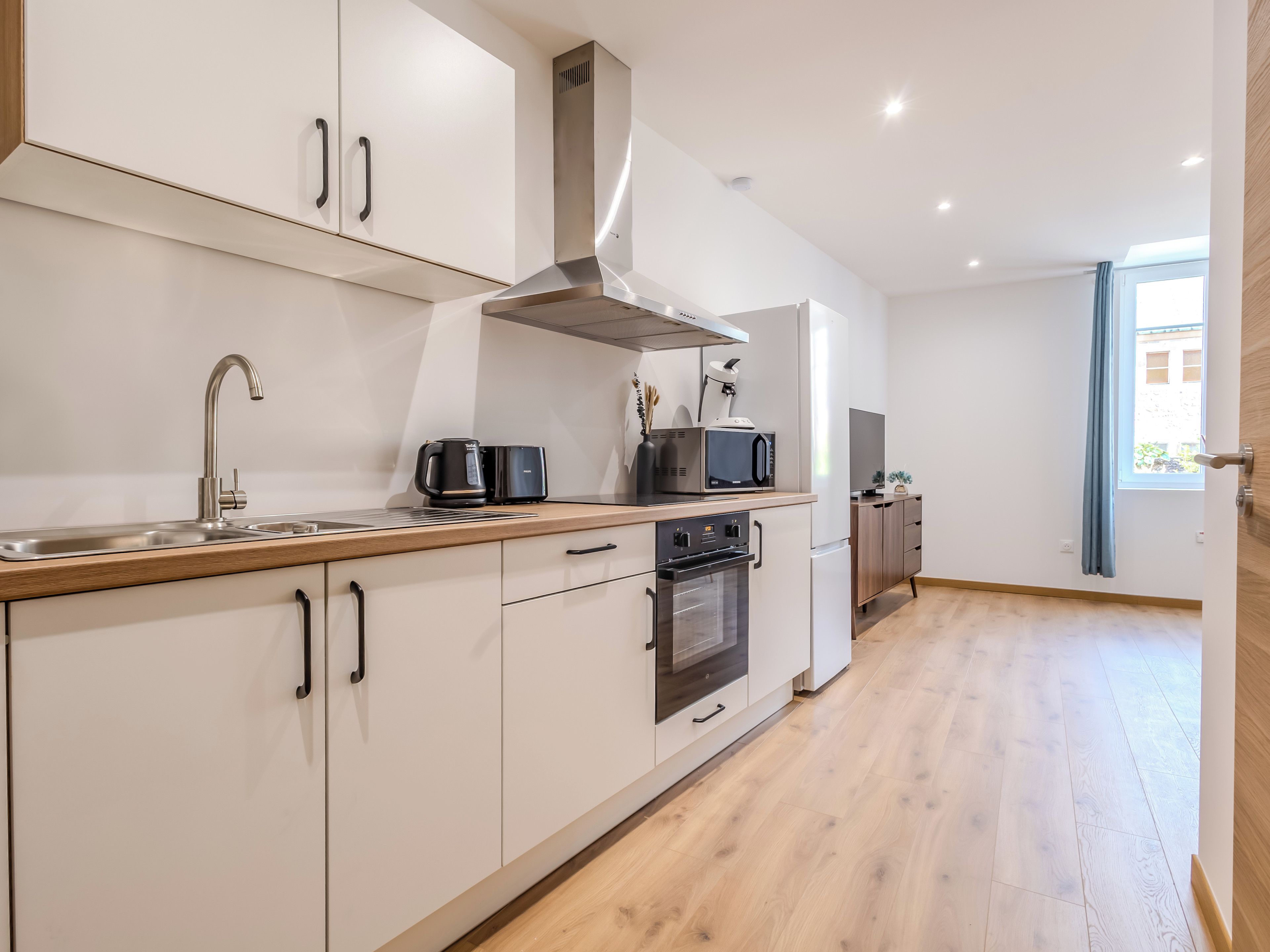 A modern kitchen with a stainless steel sink, black coffee maker, microwave, and oven.