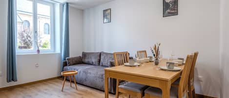 A modern living room with a sofa, dining table, chairs, and a window with curtains.