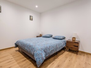 Ein Schlafzimmer mit einem Bett, zwei Nachttischen, einem kleinen Tisch daneben und einer Wandleuchte.