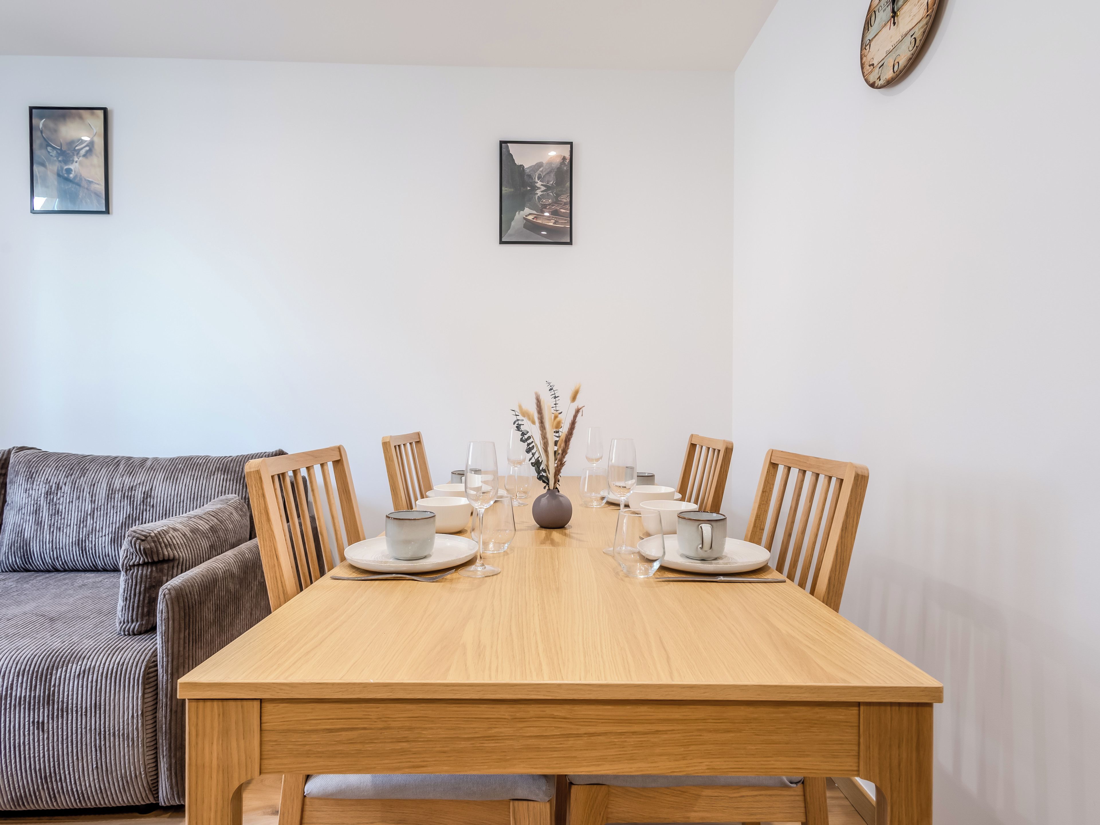 Un comedor con una mesa de madera dispuesta para seis personas, rodeada de sillas de madera. Hay dos cuadros enmarcados en la pared sobre la mesa.