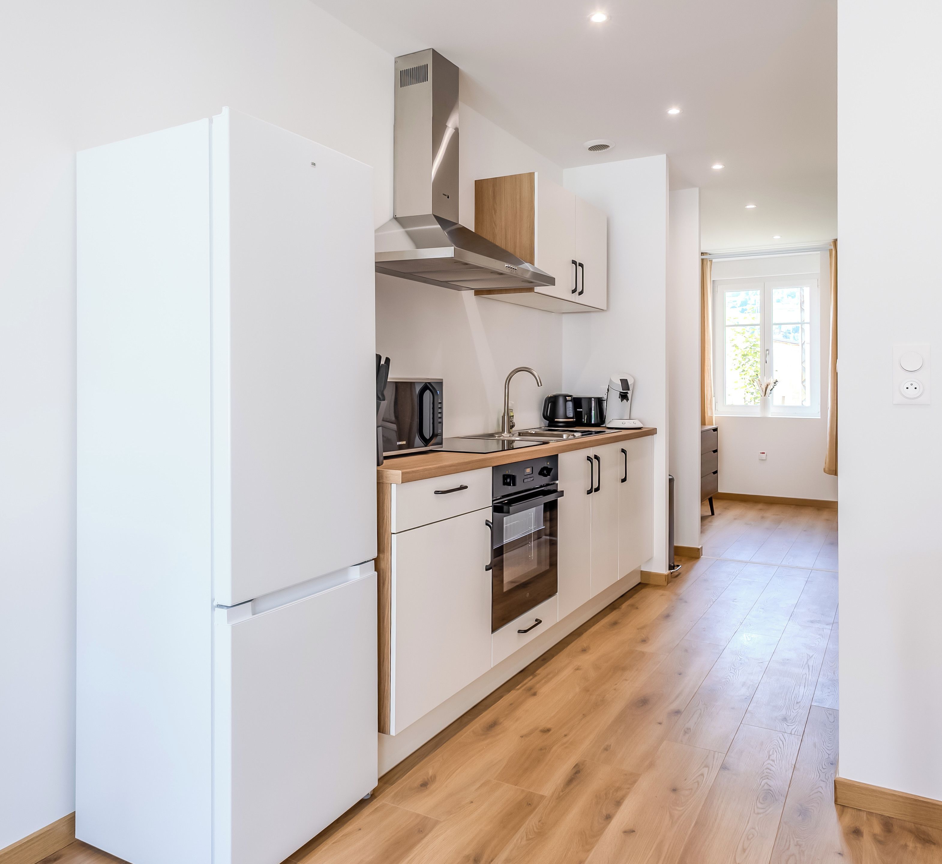 A modern kitchen with white cabinetry, a stainless steel range hood, and a built-in oven.