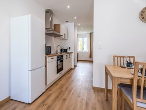 A modern kitchen with white cabinetry, a built-in oven, and a dining area with a wooden table and chairs. - Secret du Lac - Gérardmer, Vosges (Gérardmer)