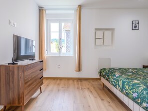 A bedroom with a wooden dresser, a bed with a floral bedspread, a window with curtains, and a wall-mounted air conditioning unit. - Secret du Lac - Gérardmer, Vosges (Gérardmer)