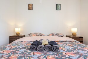 Ein ordentlich bezogenes Bett mit aufgerollten Handtüchern, zwei Nachttischlampen und einer Bettdecke mit Blumenmuster.