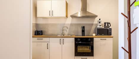 A modern kitchen with white cabinets, a stainless steel range hood, a built-in oven, and a microwave.
