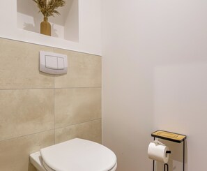 Een badkamer met een toilet, een bedieningsknop aan de muur en een toiletrolhouder.