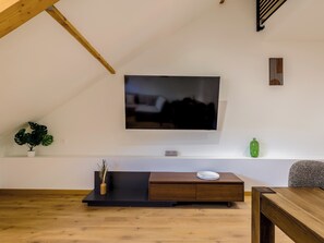Ein modernes Wohnzimmer mit Fernseher an der Wand, einer Holzbank mit einer Vase und einer Topfpflanze.