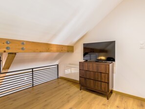 Een moderne kamer met een schuine kap, houten balken, een ingebouwde televisie en een houten dressoir.