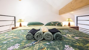 Ein ordentlich gemachtes Bett mit aufgerollten Handtüchern, einer blumigen Tagesdecke und zwei Nachttischlampen.