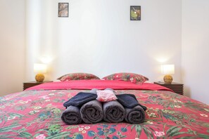 A neatly made bed with rolled towels in the center, a red floral bedspread, and two wall-mounted lamps on either side. - Écume du Lac - Gérardmer, Vosges (Gérardmer)