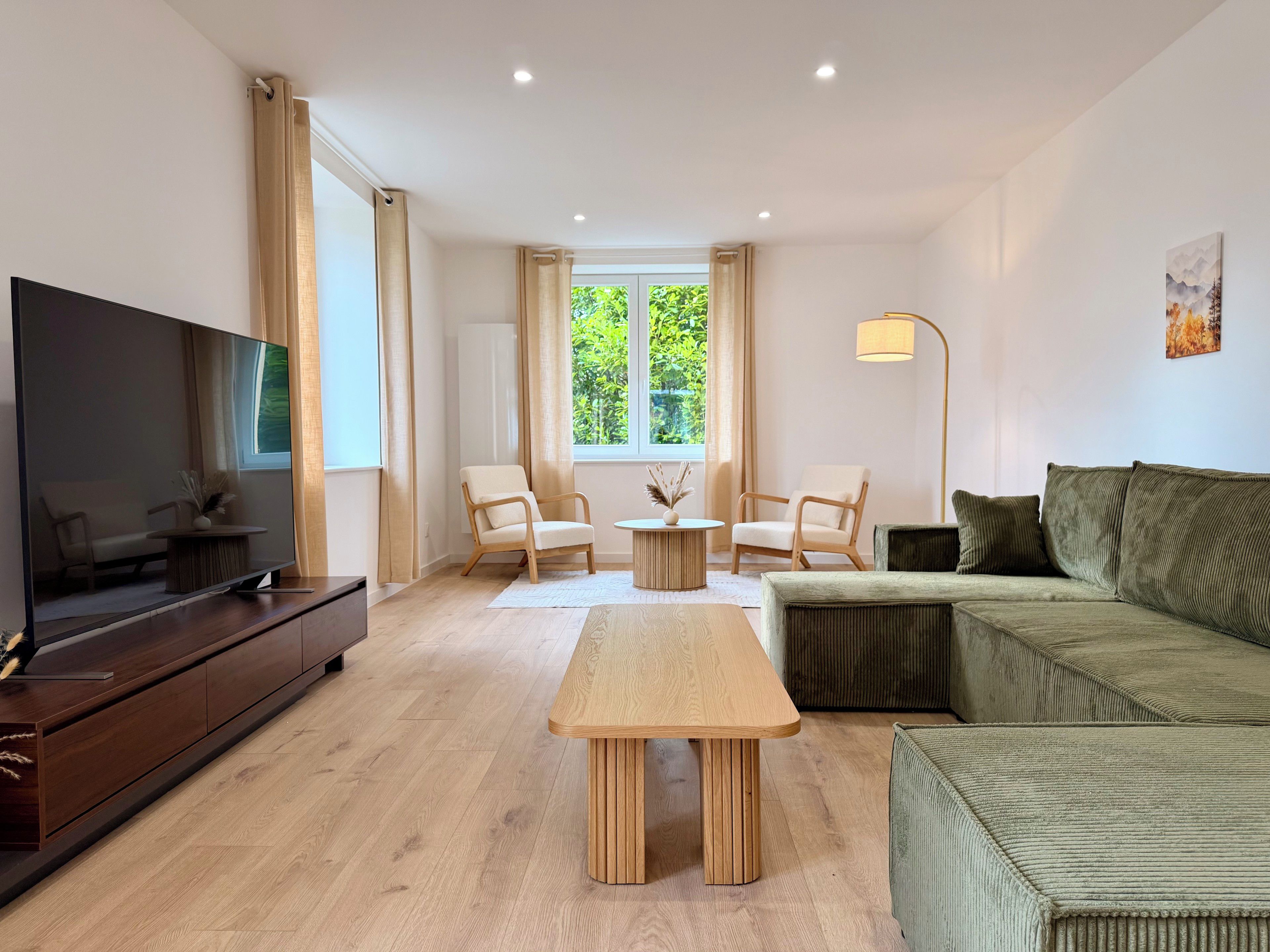 Ein modernes Wohnzimmer mit Flachbildfernseher, zwei Sesseln, einer Couch, einem Couchtisch und einer Stehlampe.