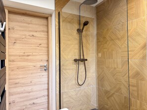 Un baño moderno con puerta de madera, ducha con cabezal de lluvia y paredes con azulejos estampados.
