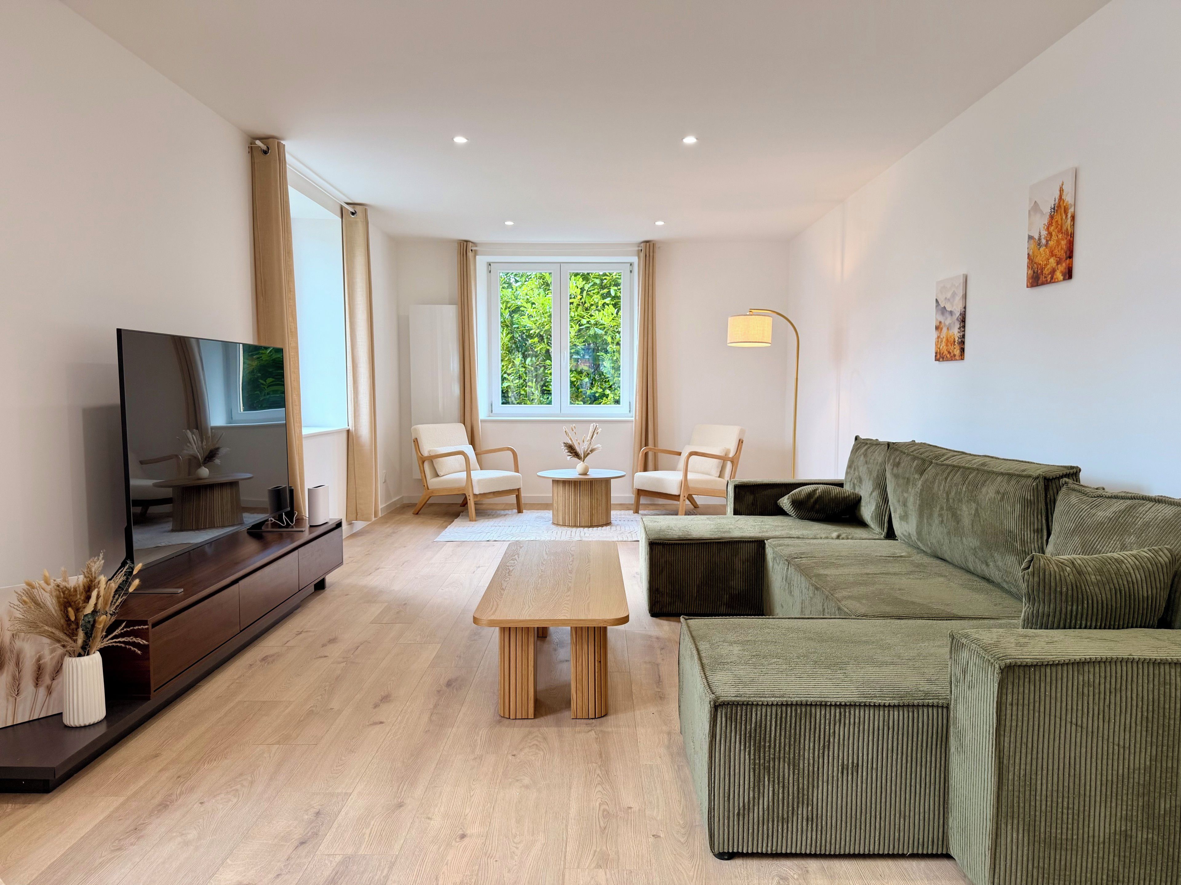 Een moderne woonkamer met een flatscreen televisie, twee fauteuils, een bank, een salontafel en een vloerlamp.