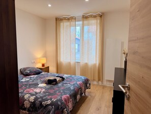 Ein Schlafzimmer mit einem Bett, einer Nachttischlampe, einem Fenster mit Vorhängen und einer Holztür.