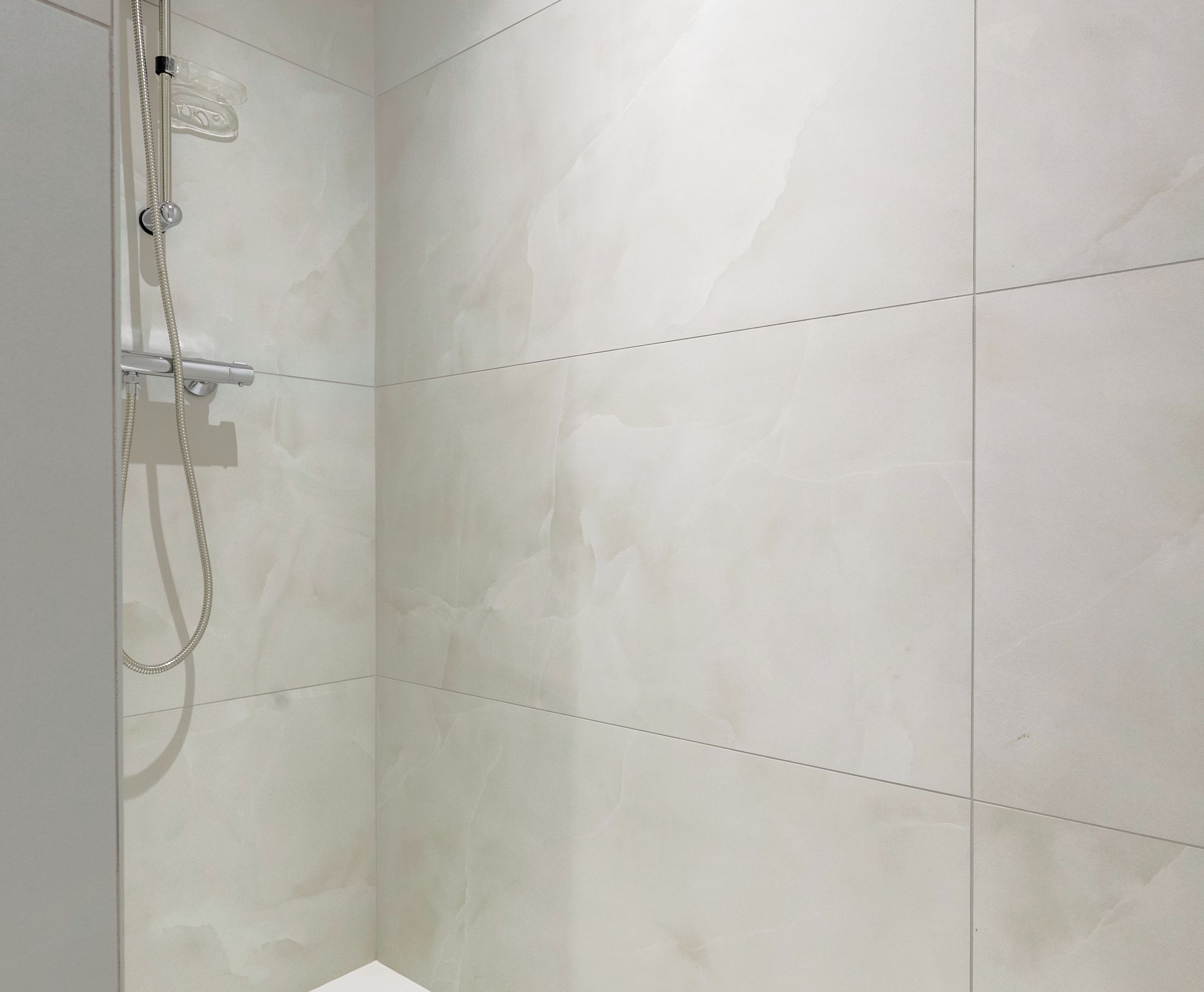 A shower area with a handheld showerhead and a wall-mounted control panel.