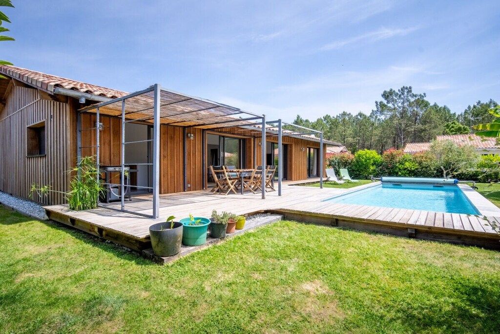 Ein modernes Haus mit überdachter Terrasse, Swimmingpool und gepflegtem Rasen.