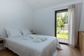 Ein Schlafzimmer mit einem Bett, einem Nachttisch und Blick auf einen Garten durch eine Schiebetür.