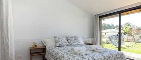 A bedroom with a large bed, a nightstand, and a view of the outdoors.