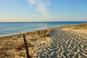 Ein Sandstrand mit einer Holzlattenveranda und blauem Himmel.