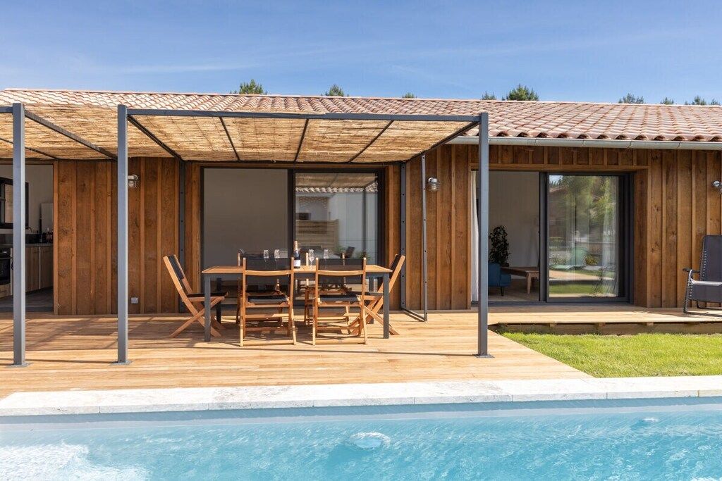 Ein Poolbereich mit überdachter Terrasse, Holzmöbeln und Blick auf den Pool.