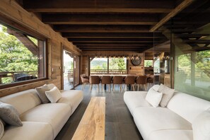 Ein modernes Interieur mit Holzbalken, einem Essbereich mit Stühlen und einem großen Fenster mit Blick auf Grünflächen.