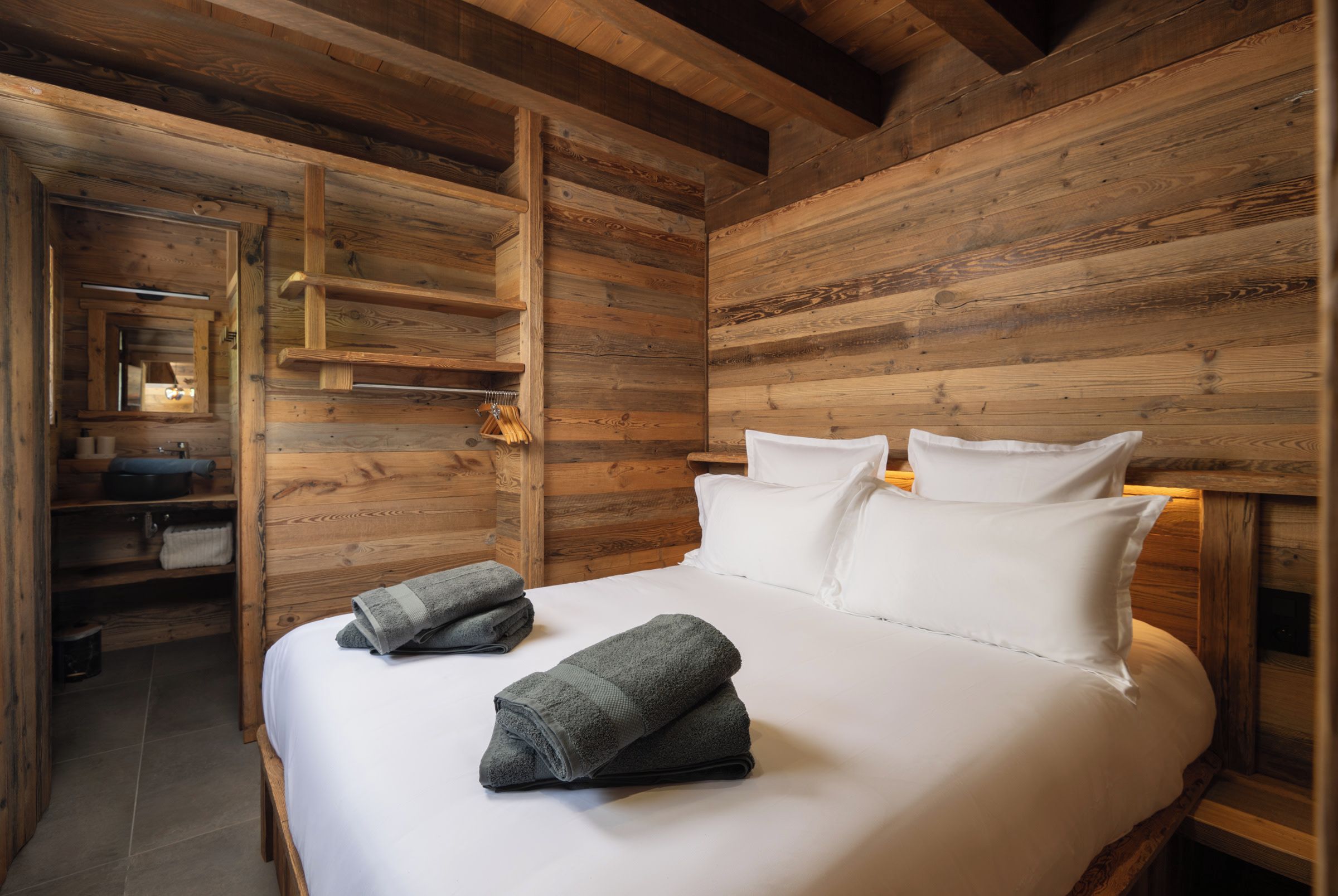 Une pièce en bois avec un lit, des oreillers et une étagère où sont rangées des serviettes.