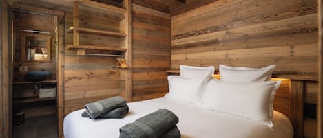 Une pièce en bois avec un lit, des oreillers et une étagère où sont rangées des serviettes.