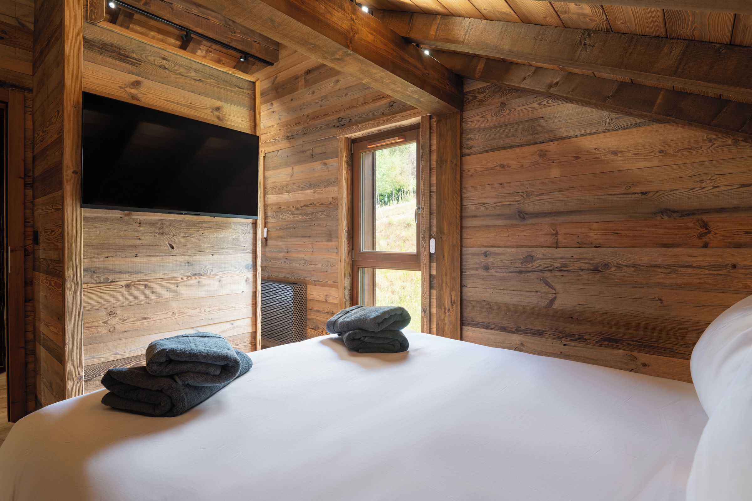 A wooden room with a bed, a television, and a window.