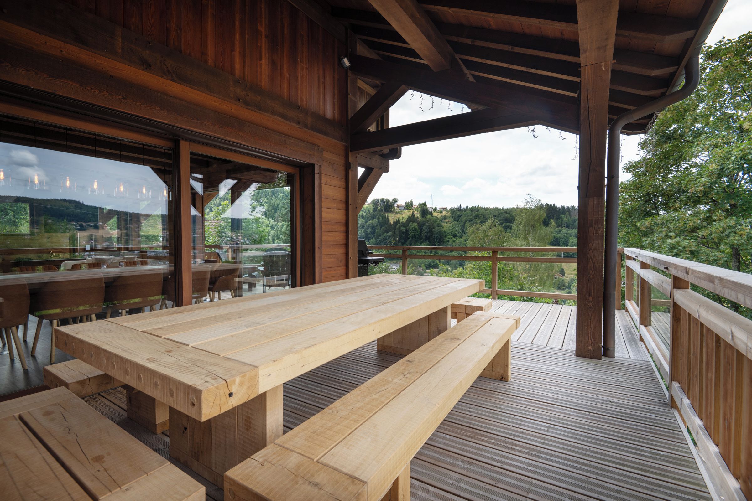 Une terrasse extérieure en bois, dotée de tables de pique-nique et offrant une vue sur un paysage boisé.
