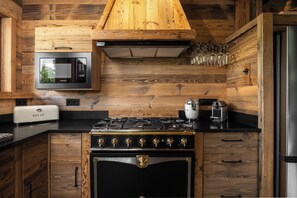 Eine Küche mit Einbau-Mikrowelle, einem Brotbackautomaten, einem Gasherd und Holzschränken.