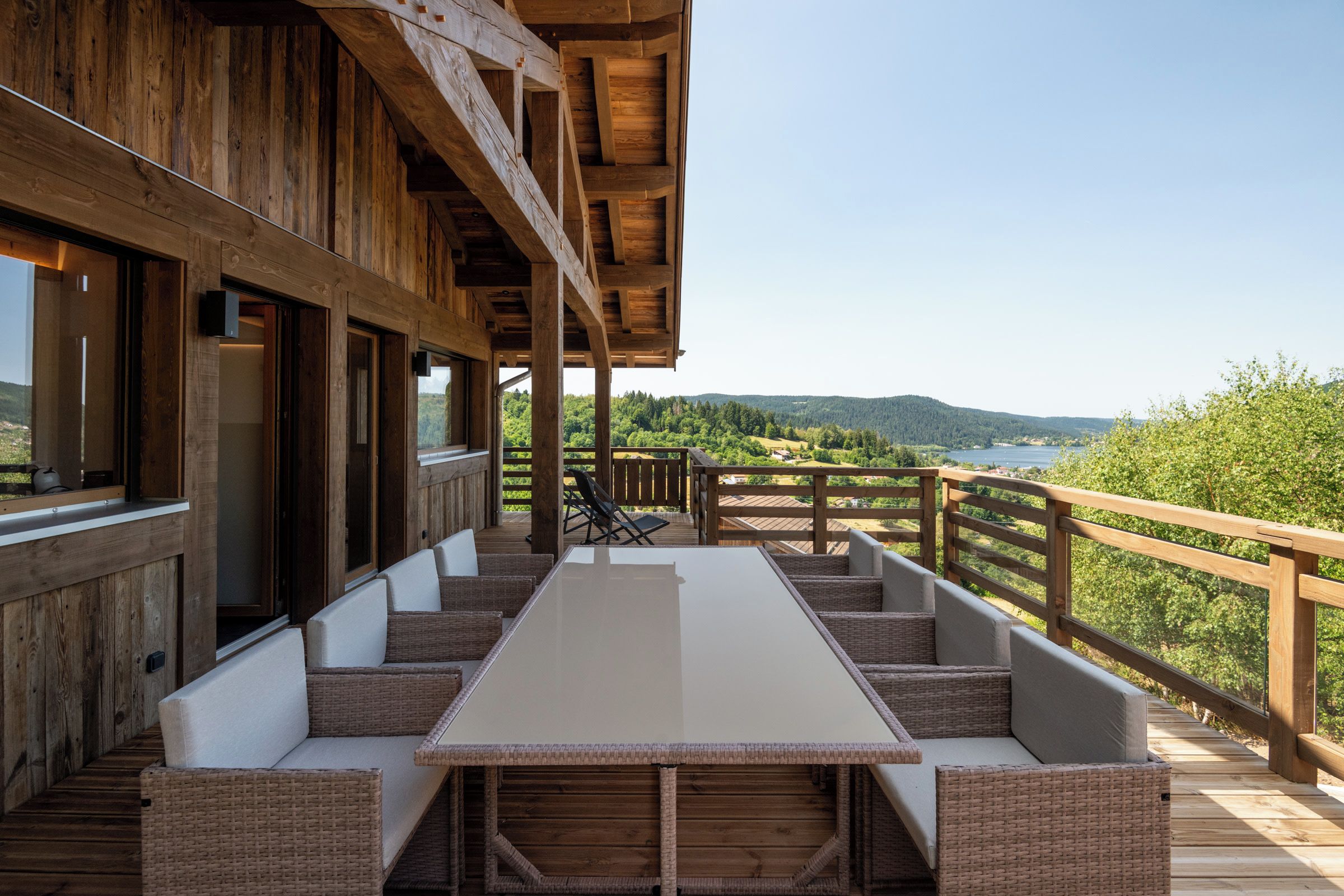 Een houten terras met een lange tafel en comfortabele zitplaatsen, met uitzicht op een prachtig landschap.