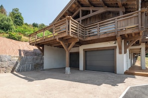 A two-story building with a wooden balcony, a garage, and a stone retaining wall. - ✨ Chalet Farnes 800 – Brand new Luxury Chalet with Panoramic Lake Views (Gérardmer)