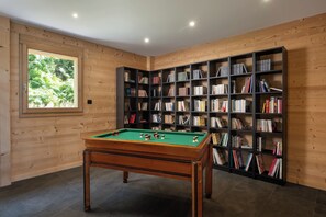 Ein Zimmer mit Billardtisch, Bücherregalen und einem Fenster mit Blick auf Grünflächen.
