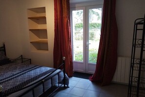 A bedroom with a bed, a built-in shelf unit, a door leading to a balcony, and a metal rack. - Holiday home with 1 bedroom (L'Isle-Jourdain)