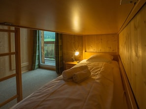 Uma cama de solteiro com cabeceira, luminária de mesa e janela com cortinas.