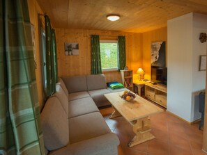 Um quarto aconchegante com sofá, mesa com uma fruteira, luminária e televisão.