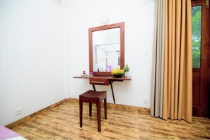 A room with a wooden desk, a chair, a mirror, and a window with curtains.