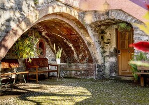 Un bâtiment rustique en pierre, doté d’une porte en bois, d’un banc et d’une table ornée de plantes en pot.