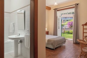 Une salle de bain avec un lavabo et une douche, et une chambre avec un lit et vue sur l’extérieur.