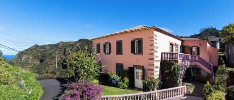 Une villa rose avec une allée sinueuse, un escalier et une vue sur la verdure et les collines environnantes.