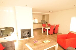 Ein Wohnzimmer mit Kamin, einem Essbereich mit roten Stühlen und einem Fernseher.