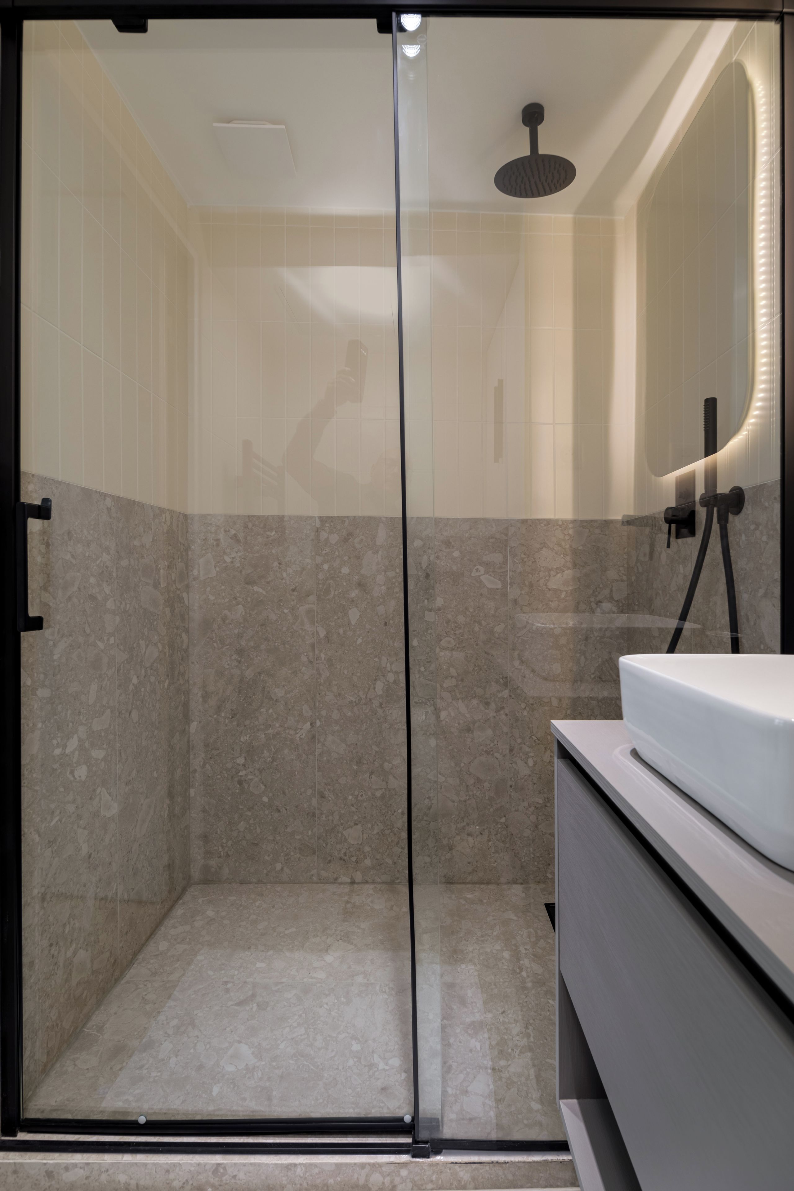A modern bathroom with a glass shower enclosure, a white sink, and a marble-tiled shower area.
