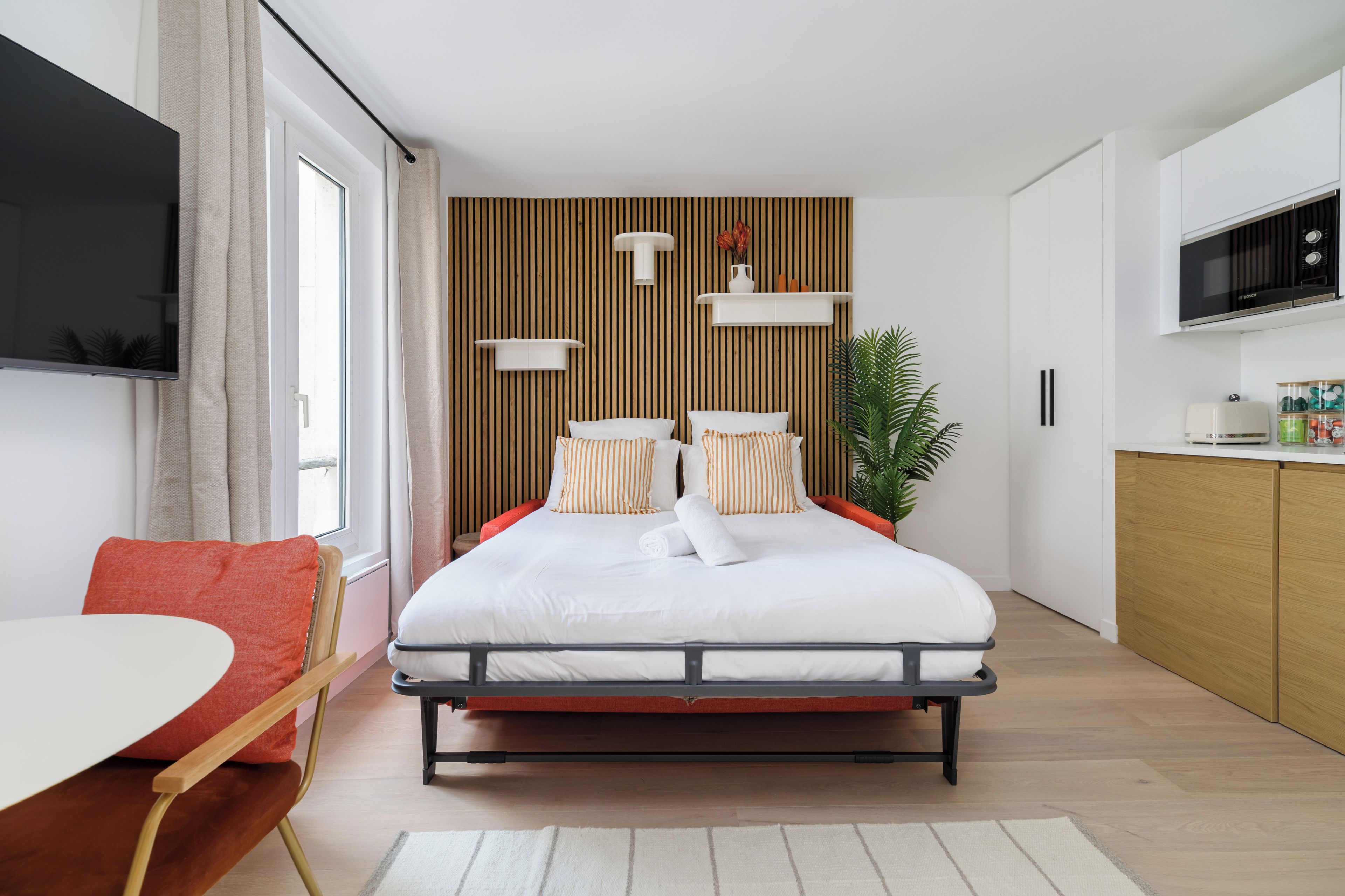 Un dormitorio moderno con cama, televisión, zona de cocina y mesa de comedor.